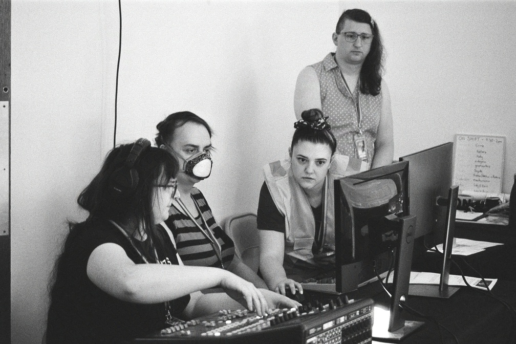Three volunteers huddle around a computer, one standing onlooking.