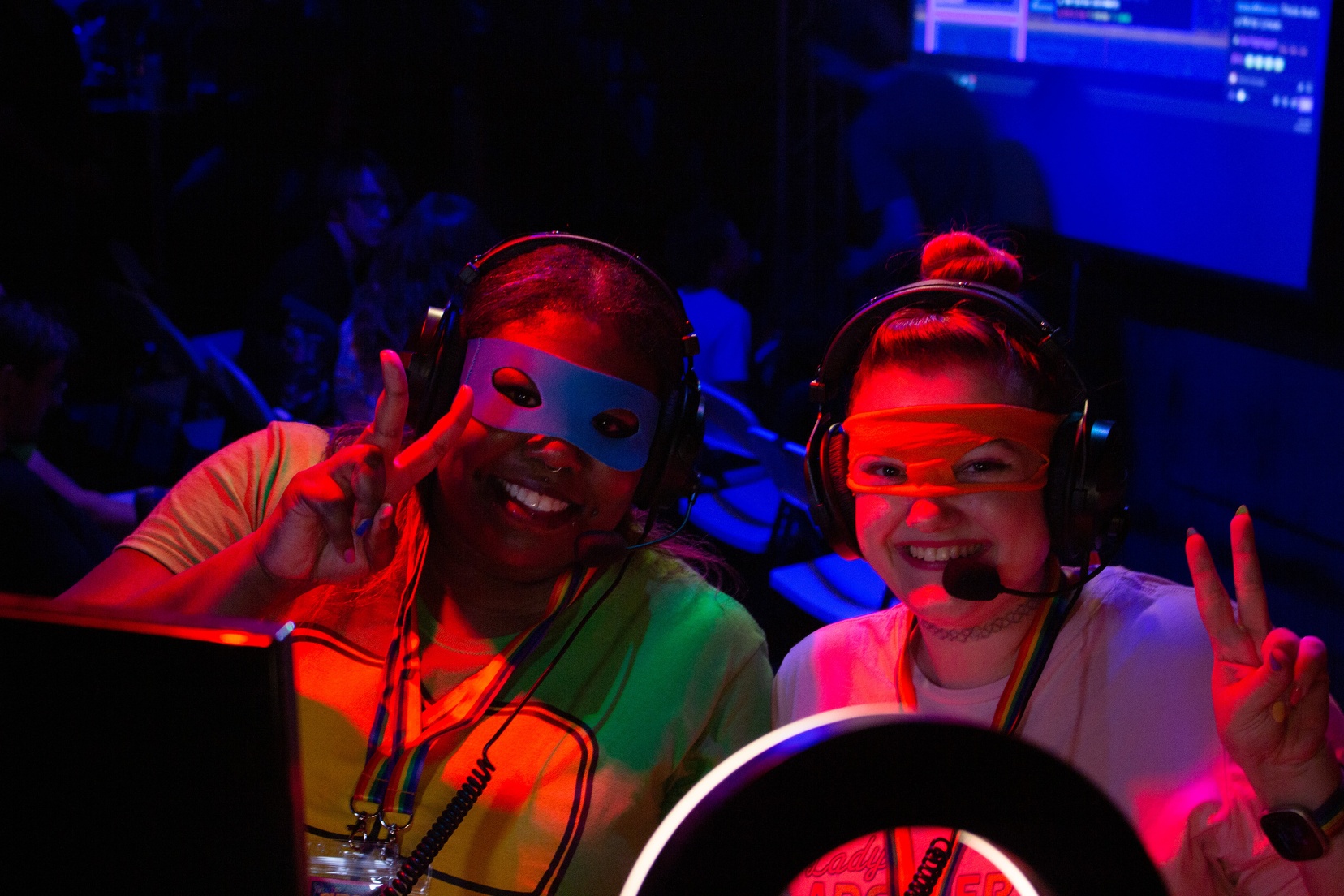 Two women smile and give peace signs while wearing Ninja Turtles masks.